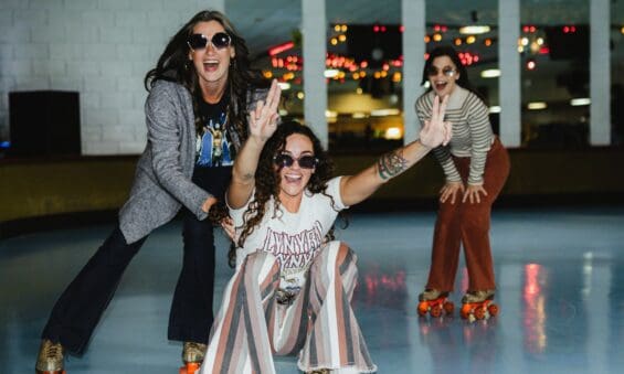 Three women in vintage-inspired outfits posing dramatically near a wall at Viking Skate Country in Redding. They're wearing roller skates and appear to be enjoying a fun, nostalgic skating session together.
